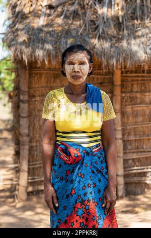 Eine madagassische Frau vor ihrer Hütte mit einem traditionell bemalten Gesicht. Madagassische Frauen malen ihre Gesichter, um sie vor der Sonne zu schützen. Stockfoto