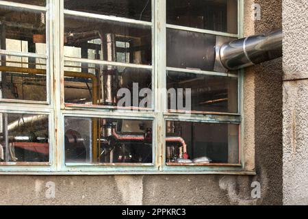 Kleines altes Heizwerk windows von außen. Heat Pipes abgedeckt in silber Folie hinter Glas sichtbar. Stockfoto