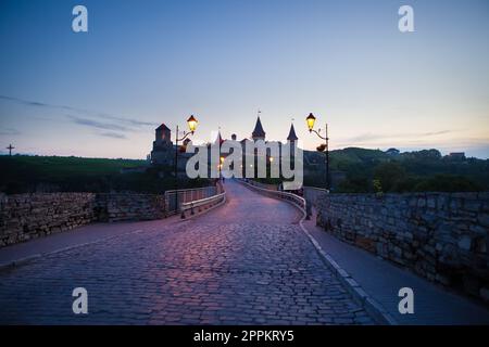 Kamianets-Podilskyi ist eine romantische Stadt, eine wunderschöne Aussicht auf die Abendstadt, Laternen beleuchten die Brücke. Ein malerischer Sommerblick auf die alte Burgfestung in Kamianets-Podilskyi, Chmelnytskyi, Ukraine. Stockfoto