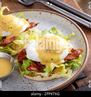 Eggs Benedict mit Speck und Salat auf englischen Muffins mit Hollandaise, traditionelle Frühstücksidee Stockfoto