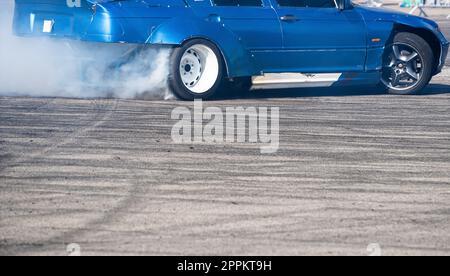 Seitenansicht eines blauen Sportwagens, der auf einer Fahrbahn mit grauer Geschwindigkeit abdriftet, wobei Rauch aus dem Hinterrad austritt Stockfoto