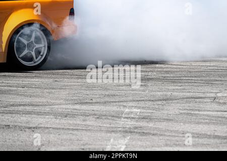 Seitenansicht eines gelben Sportwagens, der auf einer grauen Asphaltstrecke driftet, wobei Rauch aus dem Hinterrad austritt Stockfoto