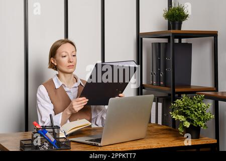 Frau mittleren Alters, die Ordner mit Akten prüft Stockfoto