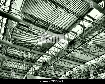 Das Dach eines Hangars, einer Produktionshalle oder einer Sporthalle. Metallkonstruktionen, Balken, Stützelemente. Lüftungsanlagen in großen Hallen und Räumen. Oberlichter. Industrieller Innenraum. Stockfoto