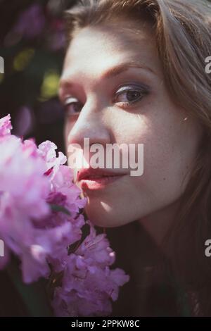 Nahaufnahme Frau, die die Wange gegen den Strauch drückt, mit pinkfarbenen Blumen im Porträt Stockfoto