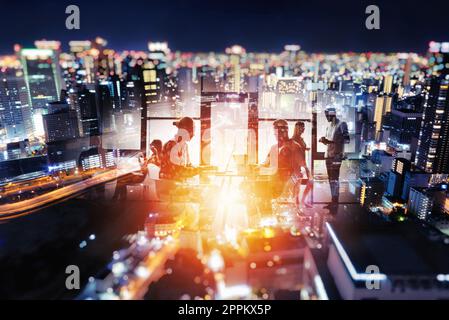 Silhouette der junge Geschäftsleute arbeiten zusammen im Büro in der Nacht auf einer Skyline im Hintergrund Stockfoto