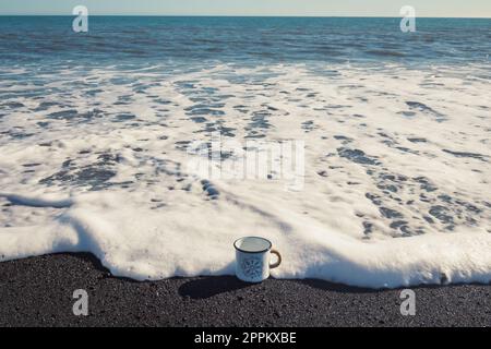 Nahaufnahme des emaillierten Bechers auf dem Sea surfline Konzeptfoto Stockfoto