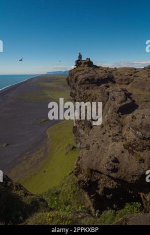 Ein Mann sitzt auf einem Landschaftsfoto von einer steilen Klippe Stockfoto