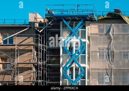 Alte mehrgeschossige Fassadenreparatur mit einem Hochscheren-Hebebühne und einer Plattform Stockfoto