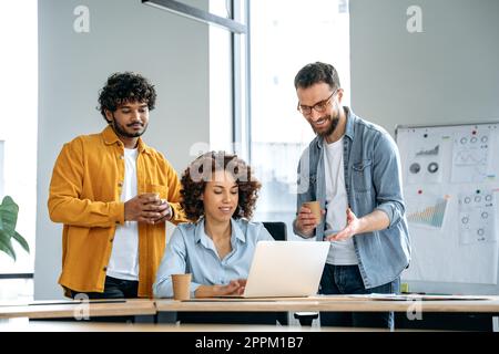Kreative Gruppe erfolgreicher Geschäftsleute aus verschiedenen Rassen, die an einem Projekt in einem modernen Büro zusammenarbeiten, Laptops verwenden, Ideen diskutieren, Brainstorming durchführen, miteinander kommunizieren, lächeln Stockfoto