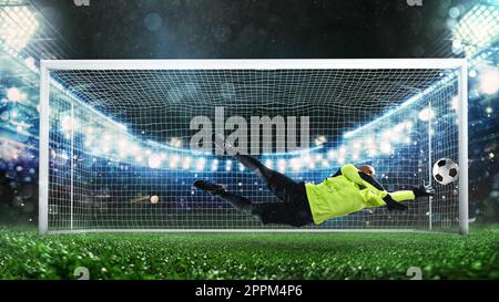 Fußball-Torwart, in fluoreszierender Uniform, das macht eine große speichern und vermeidet ein Tor während eines Spiels im Stadion Stockfoto