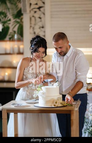 Frisch Vermählte schneiden die Hochzeitstorte gerne und kosten sie Stockfoto