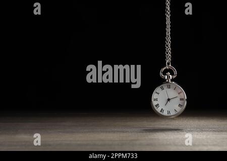 Wunderschöne Taschenuhr im Vintage-Stil mit silberner Kette auf schwarzem Hintergrund über dem Holztisch, Platz für Text. Hypnose-Sitzung Stockfoto