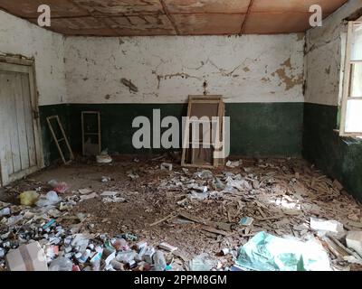 Serbien, Belgrad, 10. Mai 2020. In einem verlassenen Haus. Grunge-Szene. Verstreuter Müll auf dem Boden. Grüne Farbe an den Wänden. Weiße Halbwand. Geschossene Holzfensterrahmen. Flaschen, Papierstücke Stockfoto