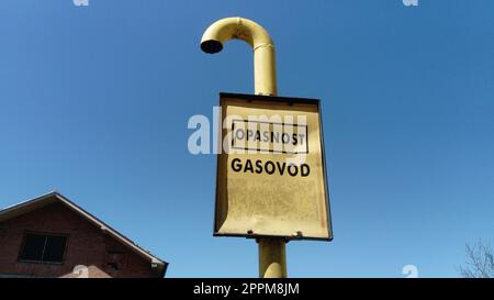 Gaszeichen mit Inschriften auf Serbisch, Montenegrin und Kroatisch - Vorsicht Gas. Zerknittertes Metallschild auf blauem Himmelshintergrund. Gasleitung durch die Landschaft. Serbien, Sremska Mitrovica Stockfoto