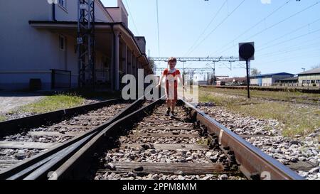 Sremska Mitrovica, Serbien, 1. Juni 2020. Ein Junge mit einer Schutzmaske läuft auf der Eisenbahn. Bahngleise und Bahnhof. Gefahr auf den Schienen. Schutz vor respiratorischen Viruserkrankungen Stockfoto