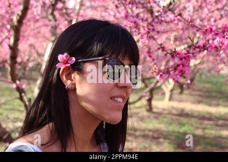 Gesicht einer jungen, schönen Frau mit pinkfarbenen Blumen, Pfirsichbaum im Haar. Stockfoto