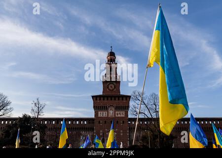 Flagge mit gelb-blau gestreiften Farben der Ukraine, die im Wind mit blauem Himmel und Sonne winkt. Im Hintergrund das Castello Sforzesco in Mailand. Stockfoto