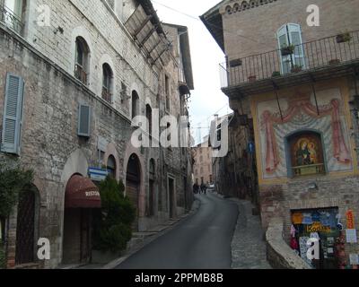 Assisi, Italien, 10. Dezember 2020. Straßen von Assisi, entlang derer eine Gruppe von Touristen zu Fuß geht. Alte Gebäude, nahe beieinander. Leute auf Ausflügen. Enge Straße Stockfoto