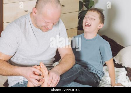 Vater spielt mit seinem Sohn 7-10 auf dem Boden. Dad kitzelt Kinderfüße. Familie, Spaß haben Stockfoto