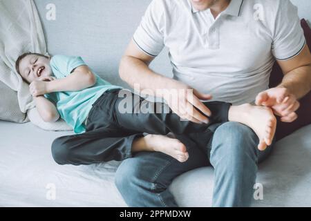 Vater spielt mit seinem Sohn 7-10 auf der Couch. Dad kitzelt Kinderfüße. Familie, Spaß haben Stockfoto