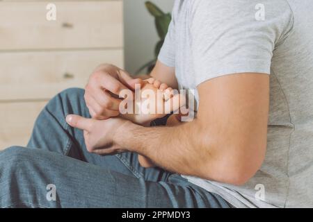 Dad hält und kitzelt die Füße des Kindes. Der Junge spielt mit seinem Vater. Familie, Spaß zu Hause Stockfoto