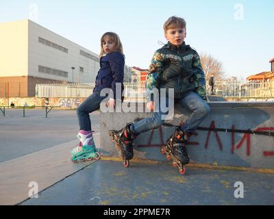 Sremska Mitrovica, Serbien, 7. März 2021. Junge und Mädchen auf Rollschuhen auf dem Sportplatz. Junge und Mädchen im Teenageralter ruhen sich nach dem Rollschuhlaufen aus. Kinder in Demi-Season-Klamotten. Stockfoto