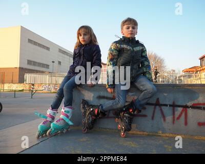 Sremska Mitrovica, Serbien, 7. März 2021. Junge und Mädchen auf Rollschuhen auf dem Sportplatz. Junge und Mädchen im Teenageralter ruhen sich nach dem Rollschuhlaufen aus. Kinder in Demi-Season-Klamotten. Stockfoto