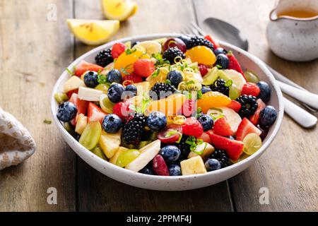 Obstsalat auf einem Holztisch mit Beeren, Zitrusschale, Minze und Honigdressing Stockfoto