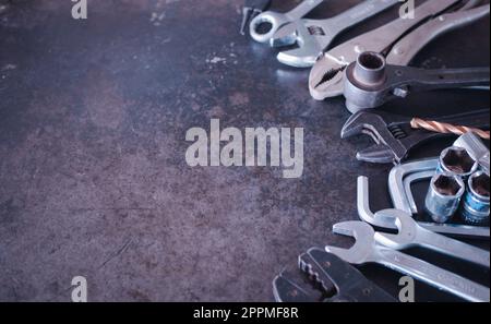 Handwerkzeuge bestehend aus Schraubenschlüsseln, Zangen, Steckschlüsseln, auf altem Stahlblechhintergrund angeordnet. Stockfoto