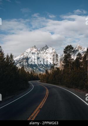 Eine kurvenreiche gepflasterte Straße zum Skigebiet Grand Targhee blickt auf den Gipfel des Grand Teton in Wyoming. Stockfoto