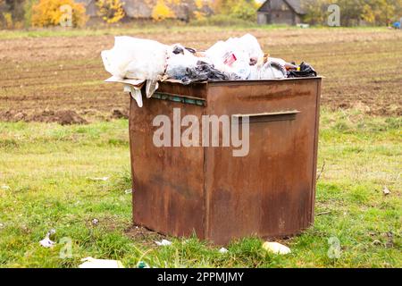 Überfließender rostiger Mülleimer auf dem Land. Müll auf dem Boden verstreut, Umweltschutz Problem Stockfoto