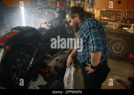 Brutaler Biker, der sich die Hände abwischte, während er den Motorradmotor reparierte Stockfoto