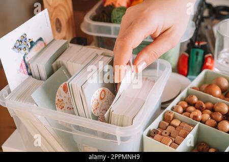 Zugeschnittenes Foto von Frauenhänden, das die Musterkarte einer transparenten Schachtel für die Lieferung der Holzperlen vorbereitet und auswählt Stockfoto