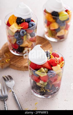 Obstsalat mit Beeren, Zitrusschale, Minze und Honigdressing, serviert in einem Glas mit einem Hauch Schlagsahne Stockfoto
