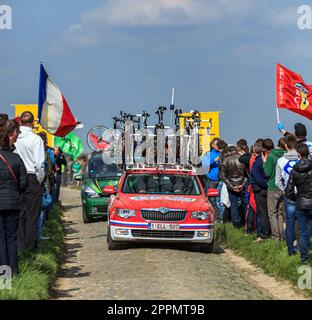 Carrefour de l'Arbre, Frankreich-April 13,2014: Reihe technischer Fahrzeuge, die den Radfahrern auf dem berühmten, staubigen Kopfsteinpflastersektor Carrefour de l'Arbr folgen Stockfoto