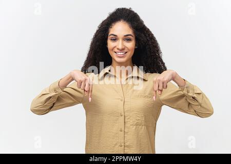 Sieh mal hier. Lächelnde, lockige, multiethnische Frau mit Afro-Haarschnitt zeigt die Finger nach unten, achtet auf Werbung, Werbetexte, Präsentation neuer Produkte, Beförderung Stockfoto