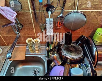 Belgrad, Serbien, 12. Dezember 2020. Küche, Ablagefläche mit Waschbecken, Draufsicht. Das Alltagsleben zu Hause. Das Geschirr ist neben dem Waschbecken gestapelt. Küchenutensilien hängen an der Fliesenwand. Sieb, Schwämme, Lappen Stockfoto