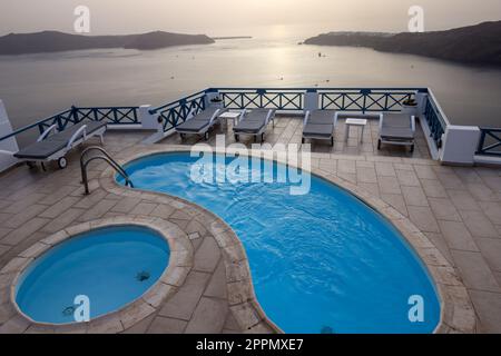 Sonnenliegen und Pools auf der Terrasse im Dorf Imerovigli mit herrlichem Blick auf den Sonnenuntergang über der Caldera in Santorin. Griechenland Stockfoto