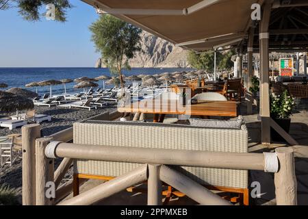 Sonnenliegen am schwarzen Vulkanstrand von Kamari in Santorini. Kykladen, Griechenland Stockfoto