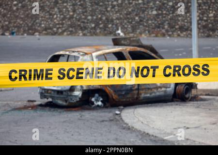 Das Auto wurde von einem Pyromanen verbrannt, mit einem Polizeivideo, auf dem steht "Verbrechensszene, nicht kreuzen". Stockfoto