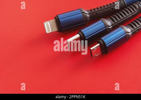 „USB-Kabel auf rotem Hintergrund“ – Nahaufnahme von USB-C-, Lightning- und Micro-USB-Kabeln mit schwarzen und blauen Farben auf rotem Hintergrund. Stockfoto