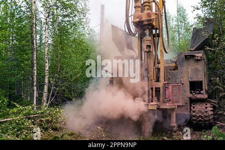 Das Kettenbohrfahrzeug bohrt gut, beim Bohren eines Brunnens ist viel Staub vorhanden. Bohren von Explorationsbrunnen im Wald. Stockfoto