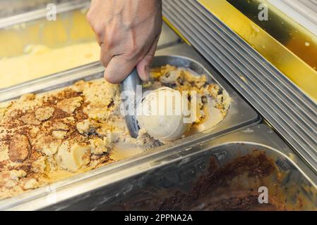 Mit der Hand eine Kugel Eiscreme in einen Löffel im Kühlschrank schöpfen Stockfoto