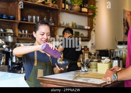 Vietnamesische Kellnerin, die einem Kunden in einem Café Eiscreme serviert Stockfoto