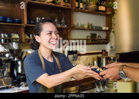 Vietnamesische Kellnerin, die einem Kunden in einem Café Eiscreme serviert Stockfoto