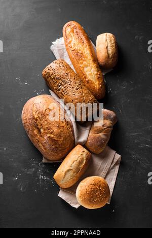 Auswahl an leckerem, frisch gebackenem Brot auf schwarzem Hintergrund. Verschiedene handwerkliche Brotzusammensetzungen. Stockfoto
