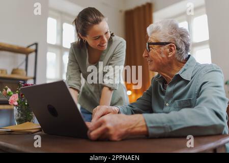 Enkelin zeigt ihrem Großvater etwas auf dem Laptop. Stockfoto