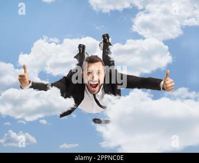 Geschäftsmann, der durch Wolken fliegt und Daumen nach oben in den Himmel streckt Stockfoto