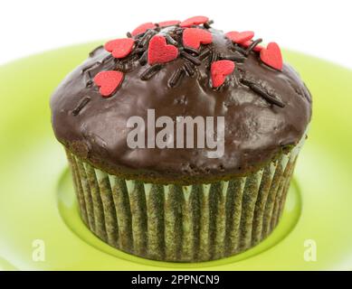 Isolierte Schoko-Muffin mit roten Zuckerherzen auf einem Teller grün Stockfoto